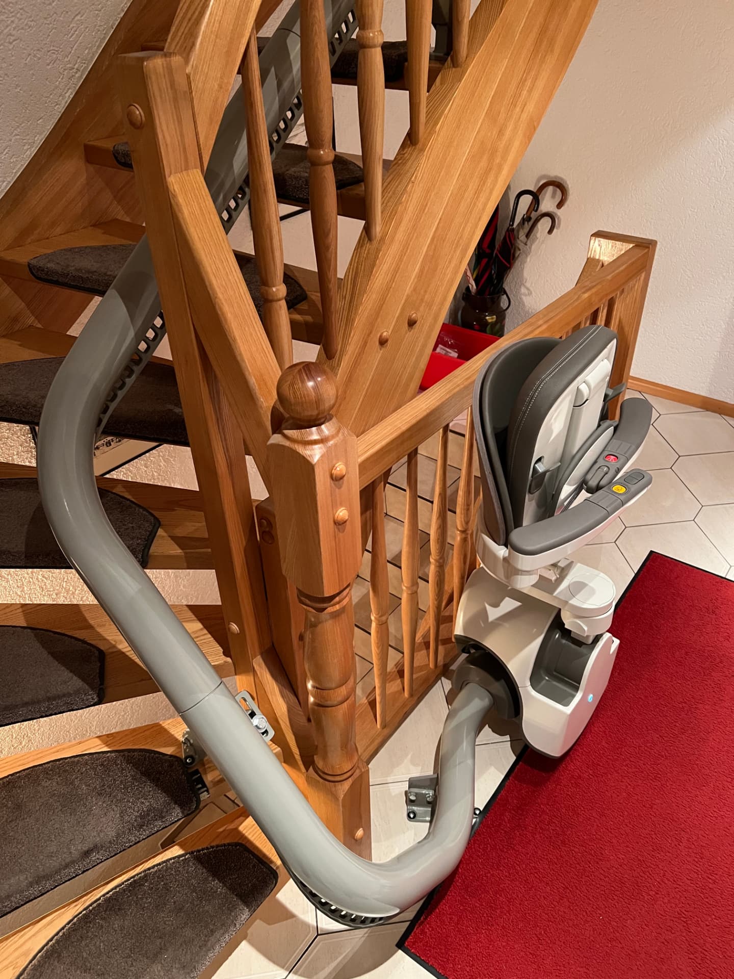 Treppenlift mit Parkposition am Fuß einer Holztreppe im Eingangsbereich